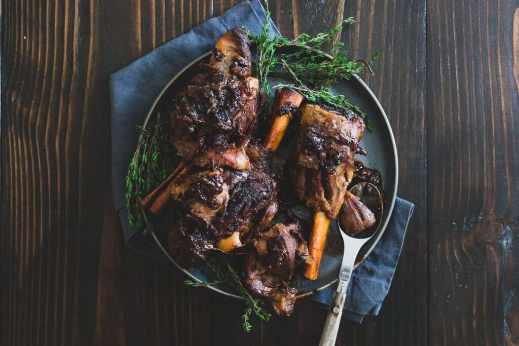 Overhead shot of braised lamb shanks on a plate with herbs and a spoon.
