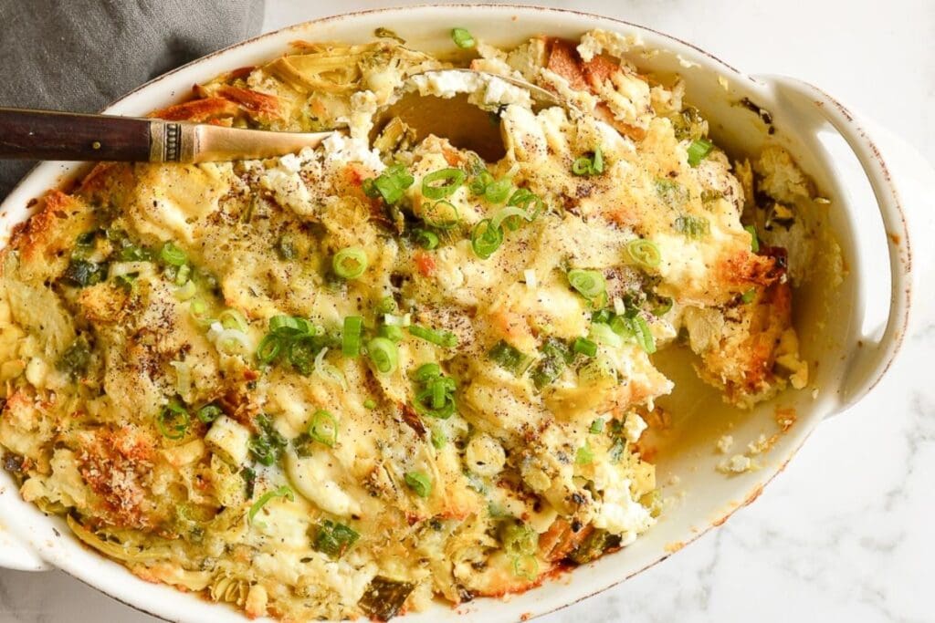 Artichoke breakfast strata with a serving spoon in a baking dish.