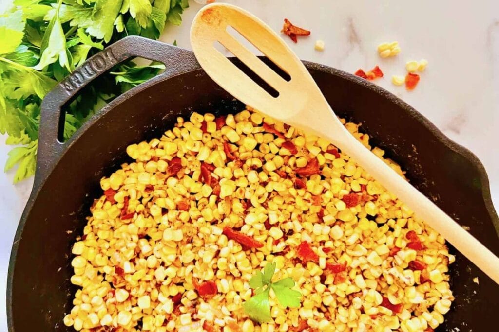 Bacon fried corn in a cast iron skillet with a wooden spoon.