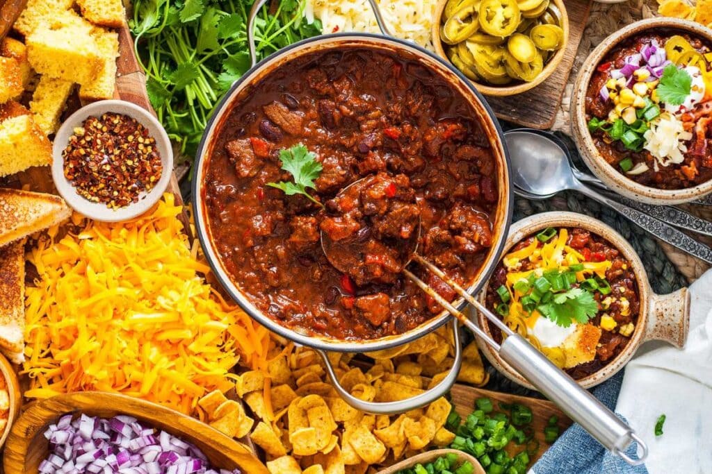 Overhead shot of beef chili with toppings like cheese, onions, cornbread, and jalapeños.
