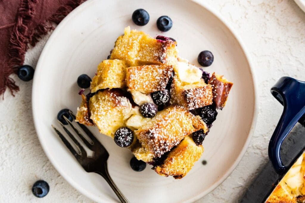 Slice of blueberry French toast casserole on a plate with a fork.