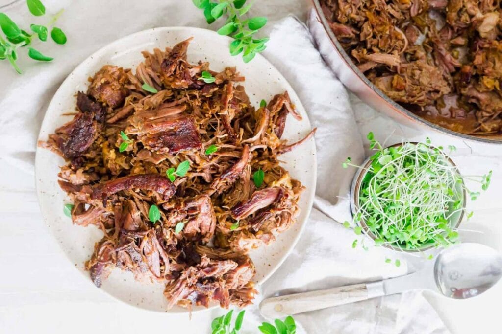 Overhead shot of braised leg of lamb on a plate with microgreens and fresh herbs.