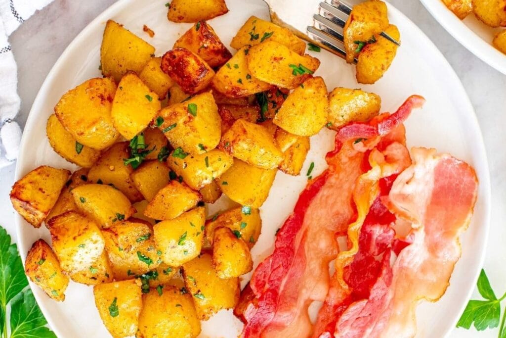 A plate of diced potatoes with herbs and crispy bacon strips.