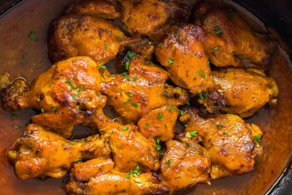 Overhead view of saucy chicken wings in a slow cooker, garnished with parsley.