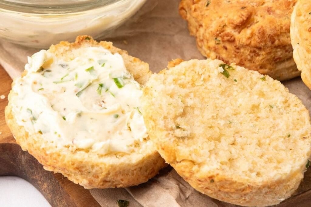 A split scone with herbed cream cheese, and other scones on a wooden board.