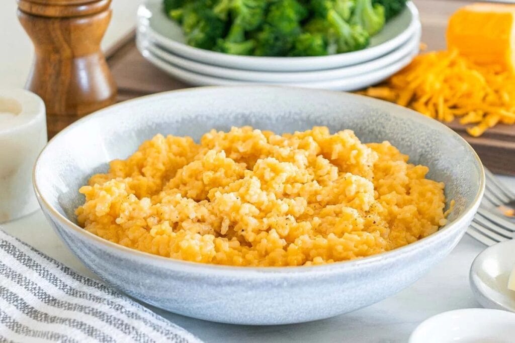 Cheesy rice in a gray bowl with broccoli in the background.