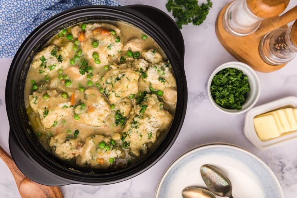 Overhead shot of chicken and dumplings in a slow cooker with butter and parsley.
