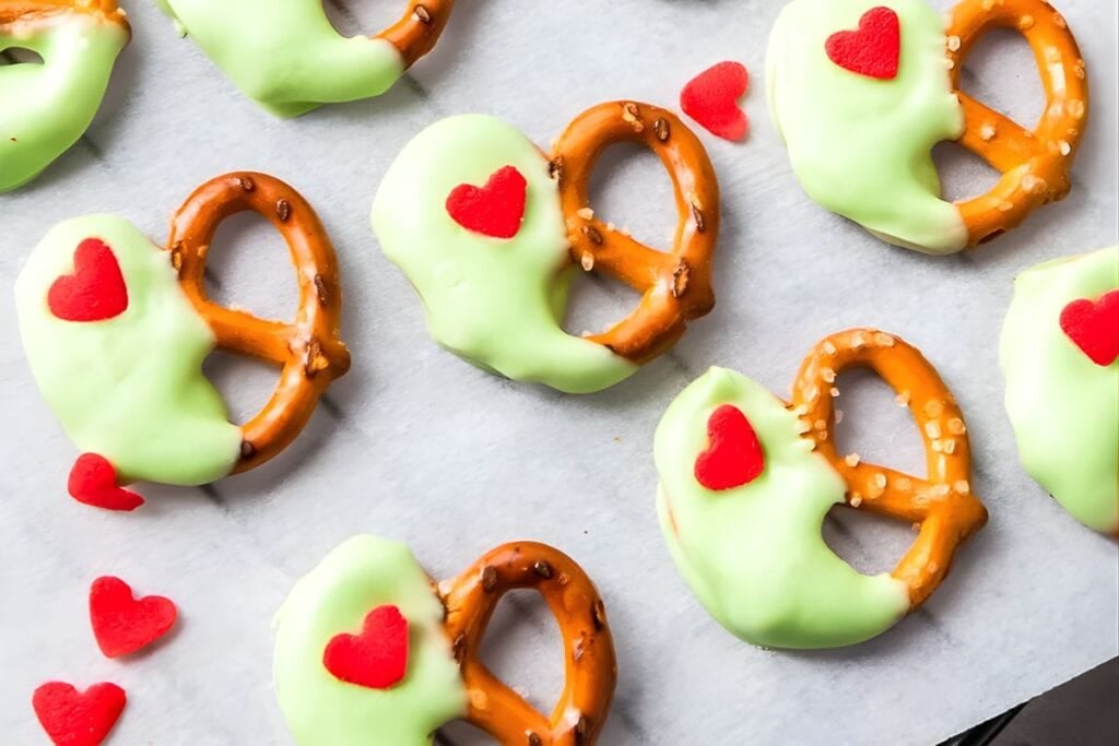 Heart-shaped pretzels dipped in green chocolate with red heart sprinkles.