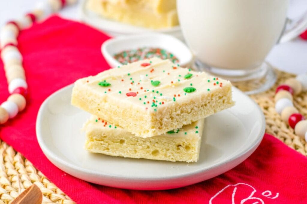 Stacked sugar cookie bars with white frosting and sprinkles on a plate.