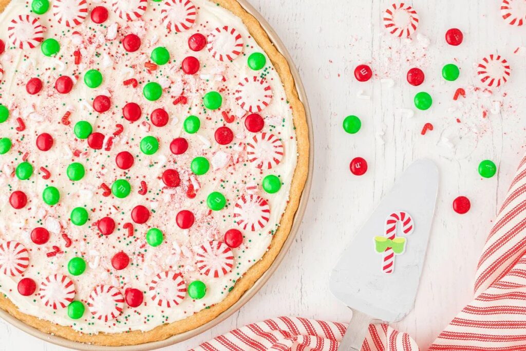 Overhead shot of a sugar cookie pizza decorated with white frosting, peppermint candies, and red and green M&Ms.
