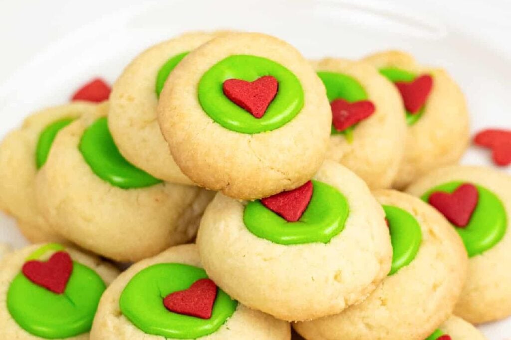 Close-up of Christmas thumbprint cookies with green icing and red hearts.