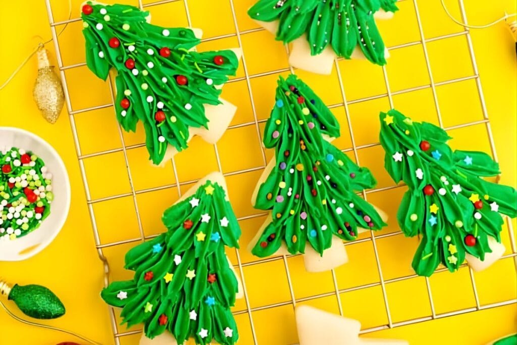 Christmas tree cookies with green frosting and sprinkles on a gold rack.