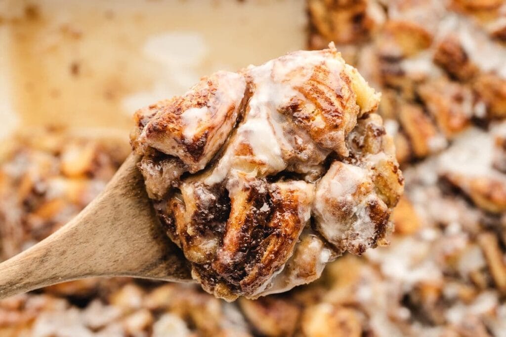 Wooden spoon holding a portion of cinnamon roll casserole with icing.