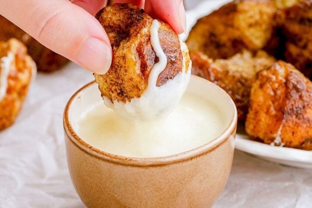 A hand dipping monkey bread into a bowl of white sauce.
