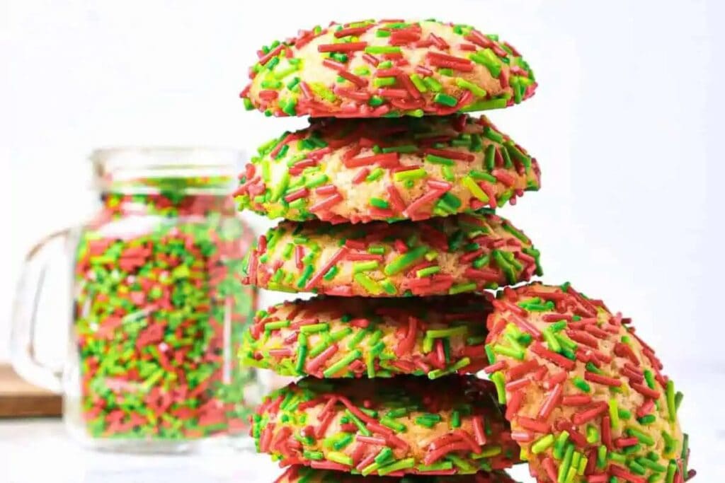 A stack of sprinkle-covered cookies and a jar of sprinkles.