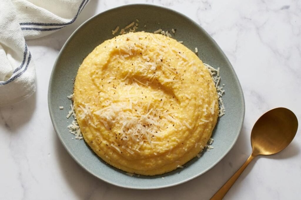 Creamy polenta with parmesan cheese and pepper on a gray plate.