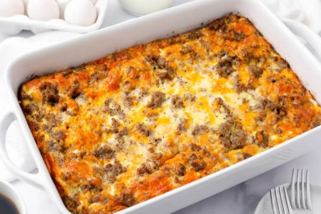 Sausage breakfast casserole in a white baking dish, with eggs and milk nearby.