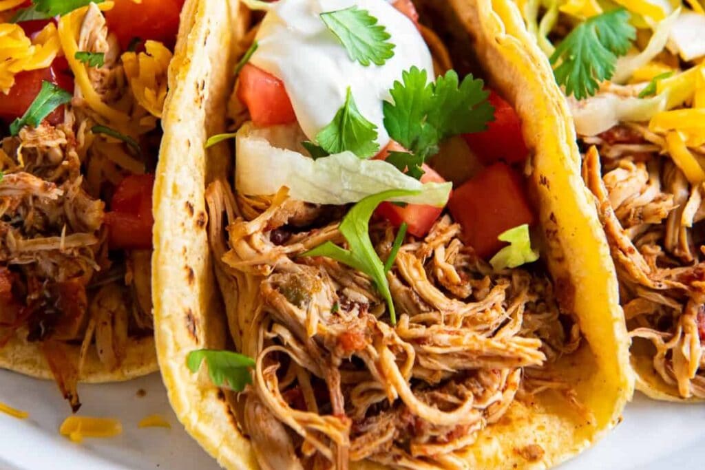 Three chicken tacos in flour tortillas, topped with cheese, tomatoes, and sour cream.