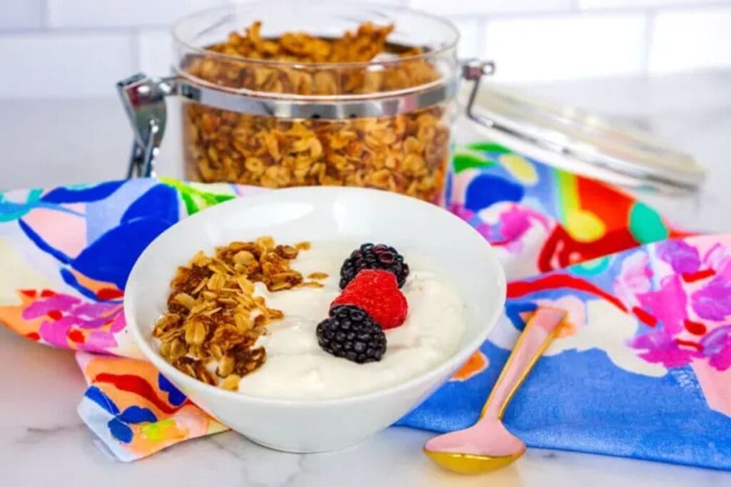 A bowl of yogurt with granola and berries, with a jar of granola behind.