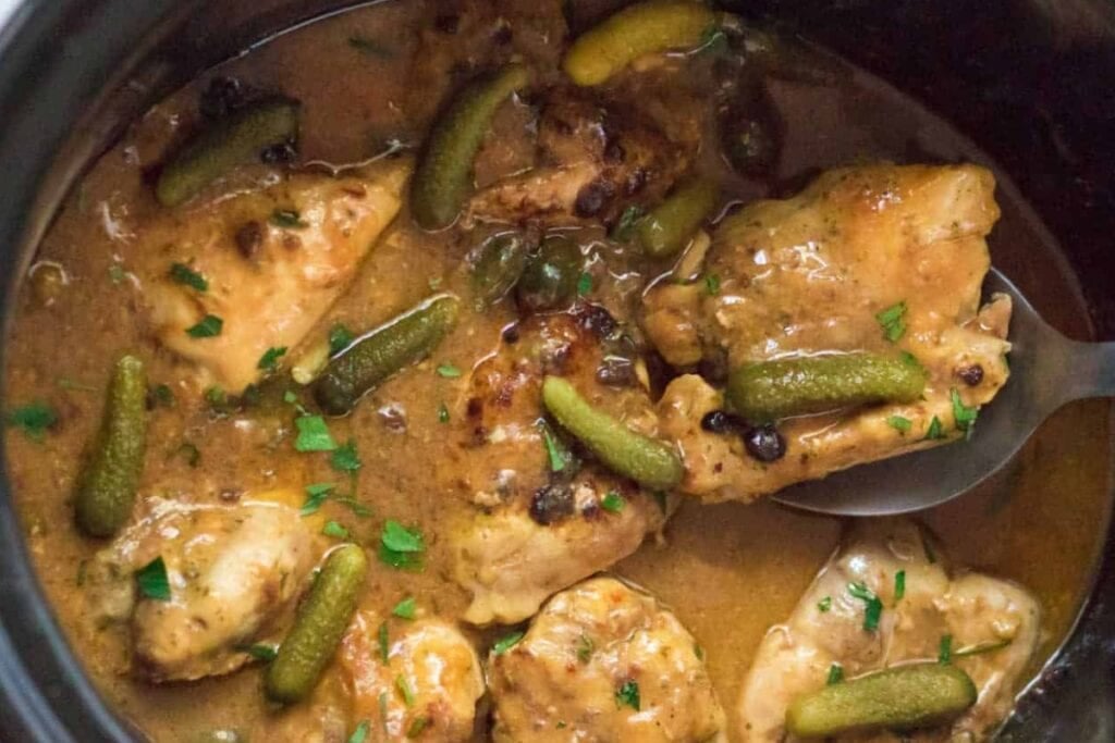 Chicken pieces in a creamy sauce with small pickles and herbs.
