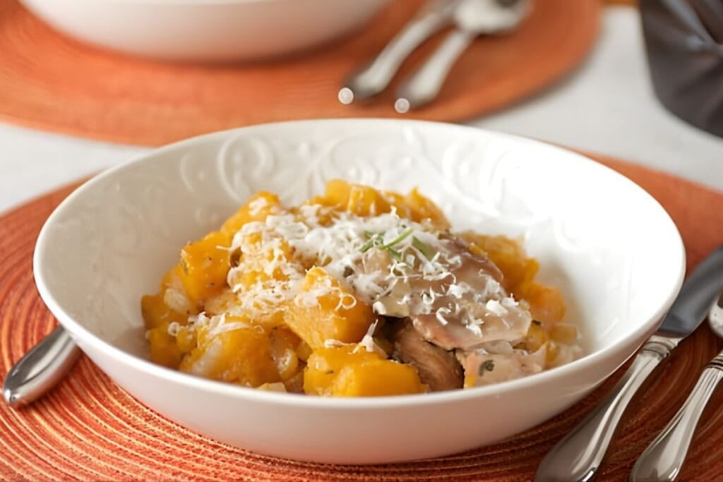 Bowl of chicken and butternut squash with parmesan cheese on an orange placemat.