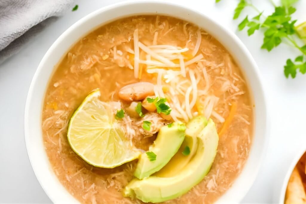 Overhead shot of white chicken chili in a bowl, topped with avocado and lime.
