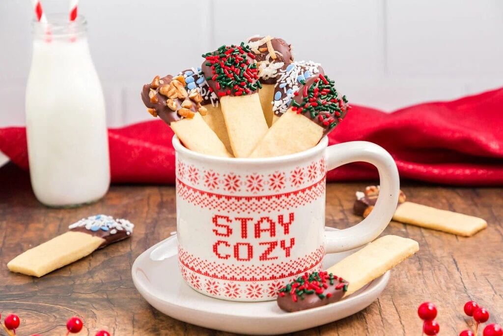 Chocolate-dipped sugar cookie sticks in a "Stay Cozy" mug with milk.