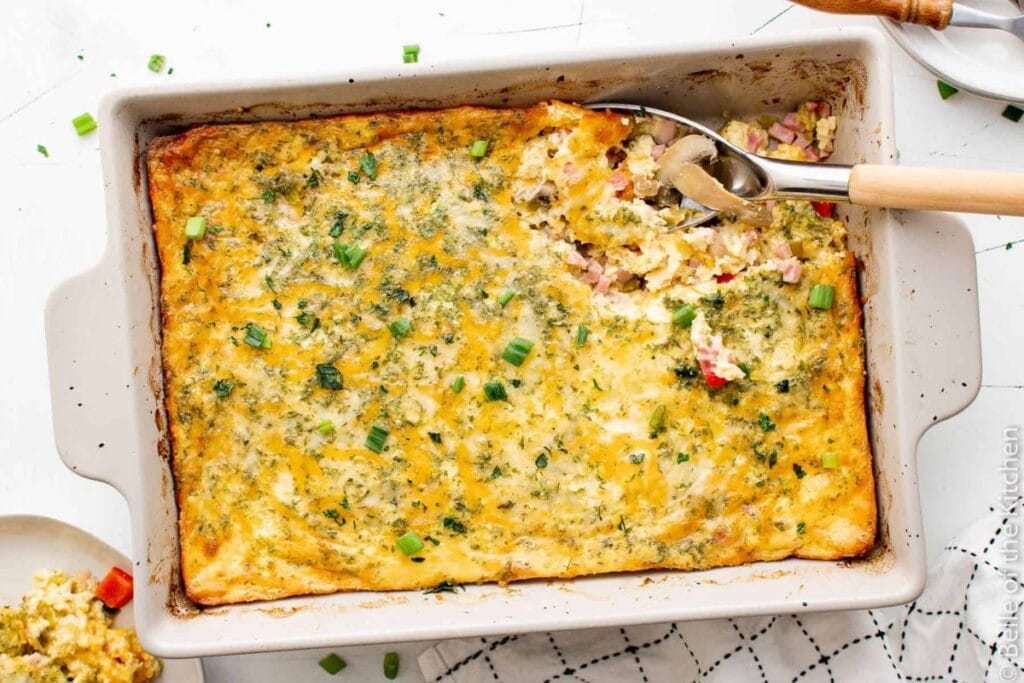 Ham, egg, and cheese casserole in a baking dish with a serving spoon.