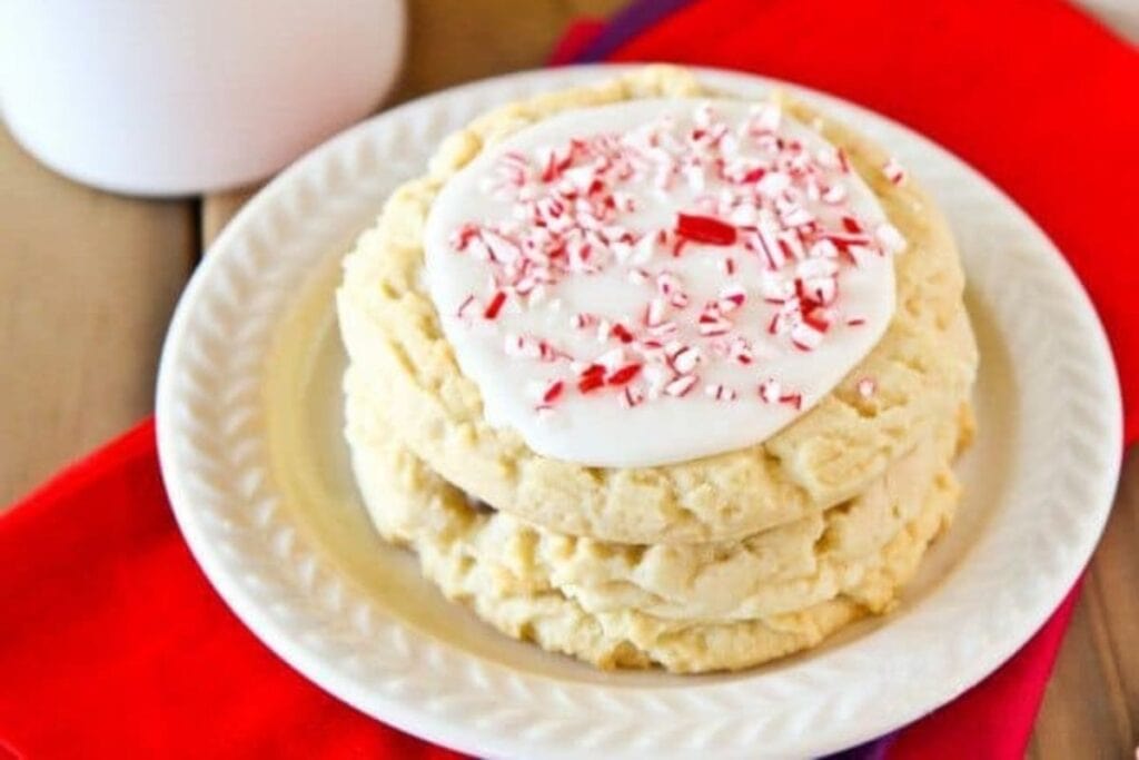 Stack of sugar cookies with white icing and crushed candy canes on a plate.