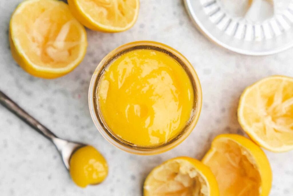 Lemon curd in a jar with squeezed lemon halves and a lemon juicer.