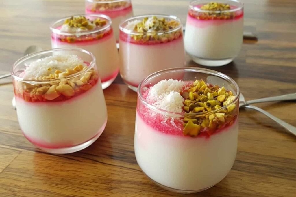 Malabi dessert cups with a white layer, red syrup, pistachios, and coconut flakes.