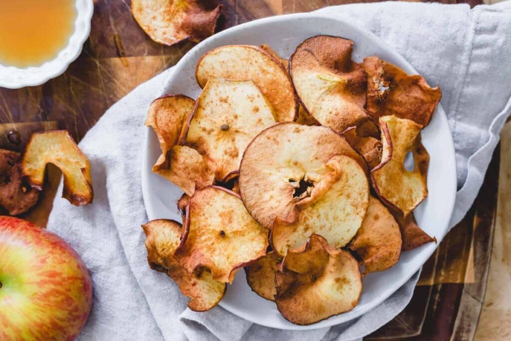 Top-down shot of apple chips in a bowl, with a raw apple nearby.