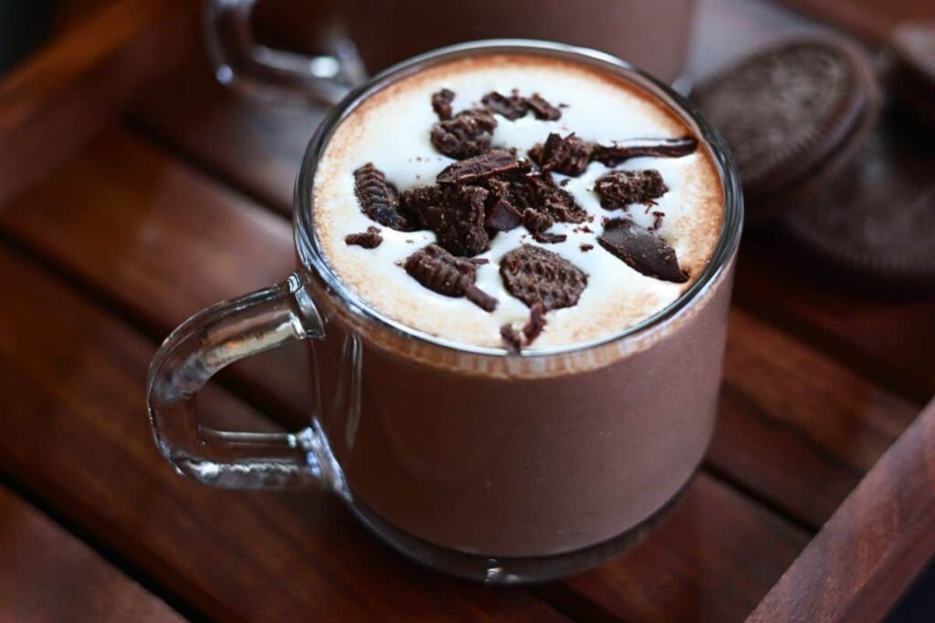 Hot chocolate with whipped cream and Oreo crumbles in a glass mug.