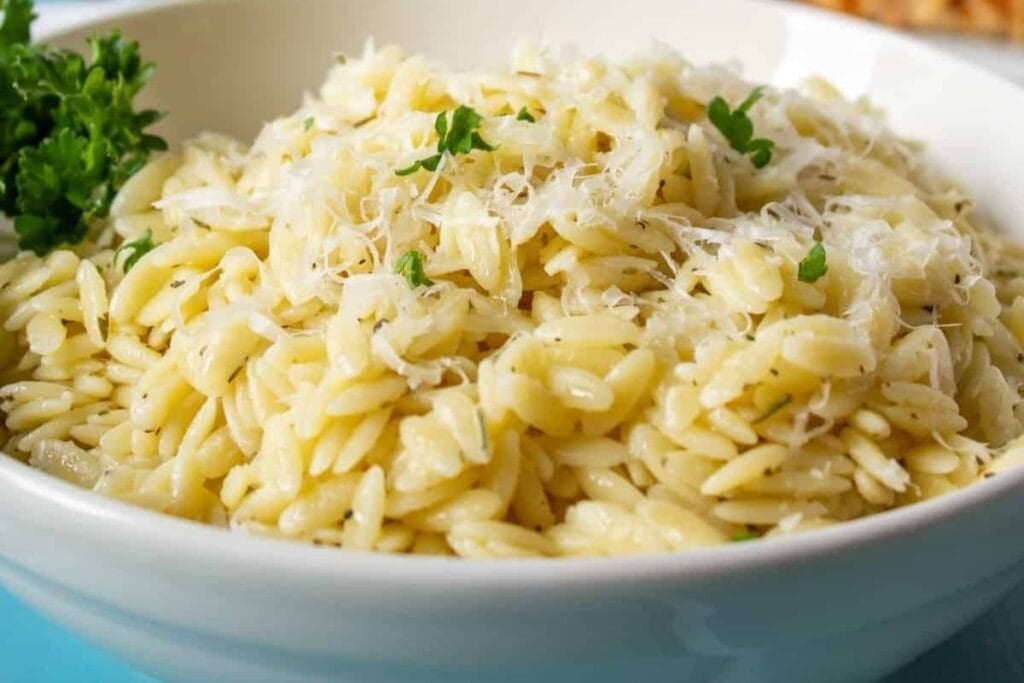 Orzo pasta with parmesan cheese and parsley in a white bowl.