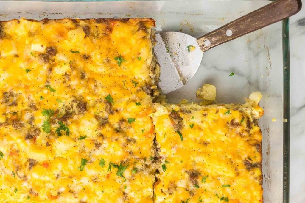 Sausage and potato breakfast casserole in a glass baking dish with a spatula.