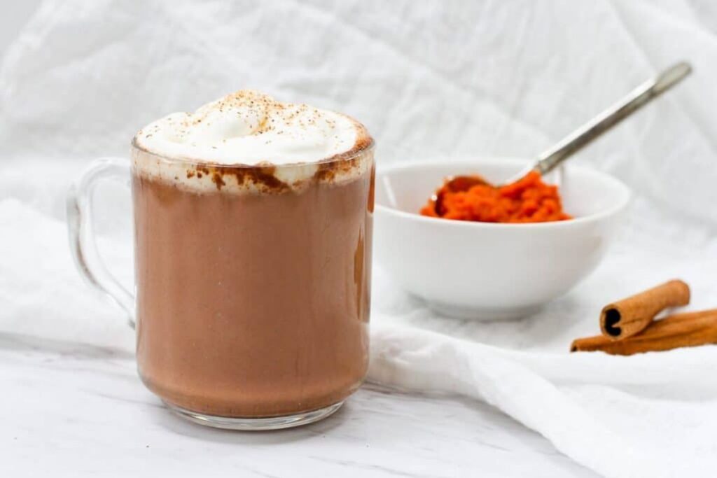 Clear mug of pumpkin spice hot chocolate with whipped cream topping.