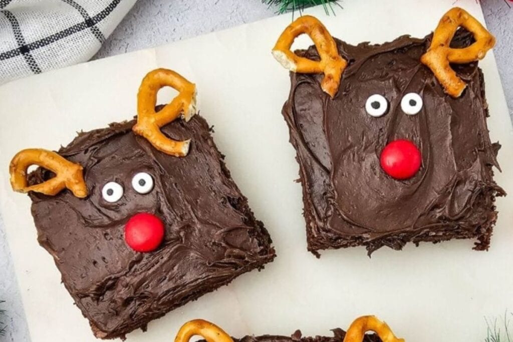 Two reindeer brownies with chocolate frosting, pretzel antlers, candy eyes, and red candy noses.