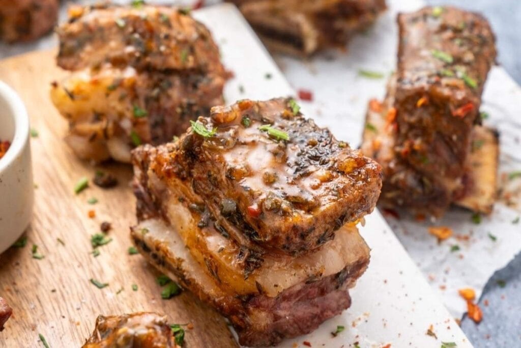 Close-up of glazed short ribs on a wooden board, garnished with herbs.