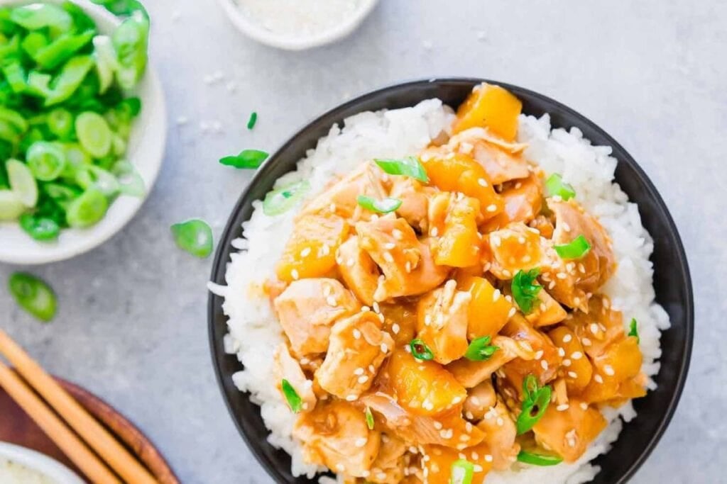 Overhead shot of chicken and mango stir-fry with rice in a black bowl.
