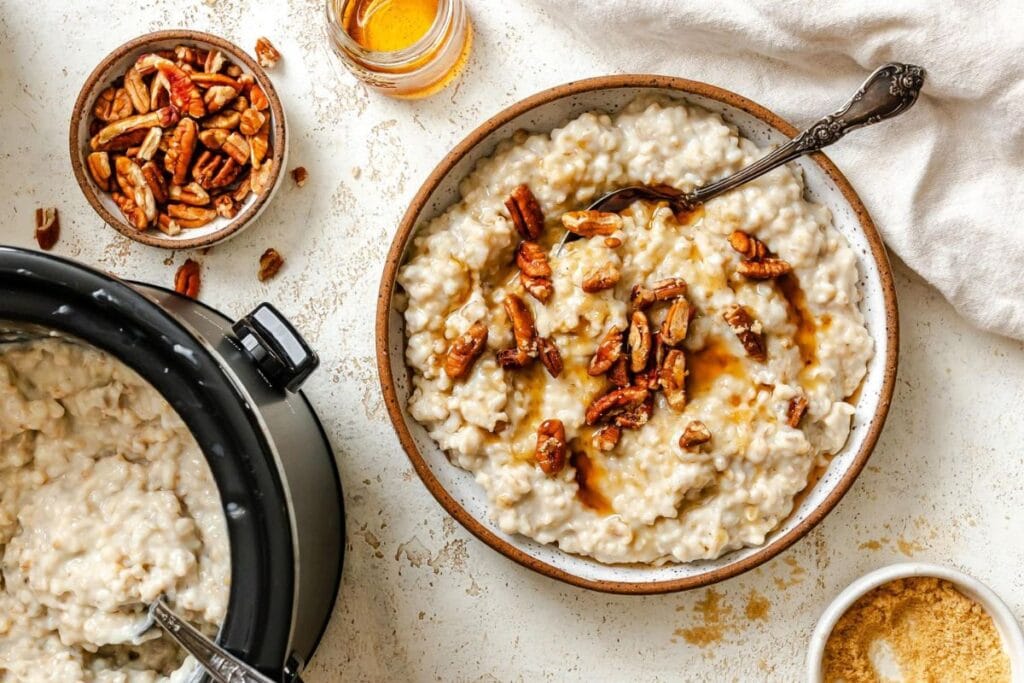 A bowl of oatmeal with pecans and honey next to a slow cooker.