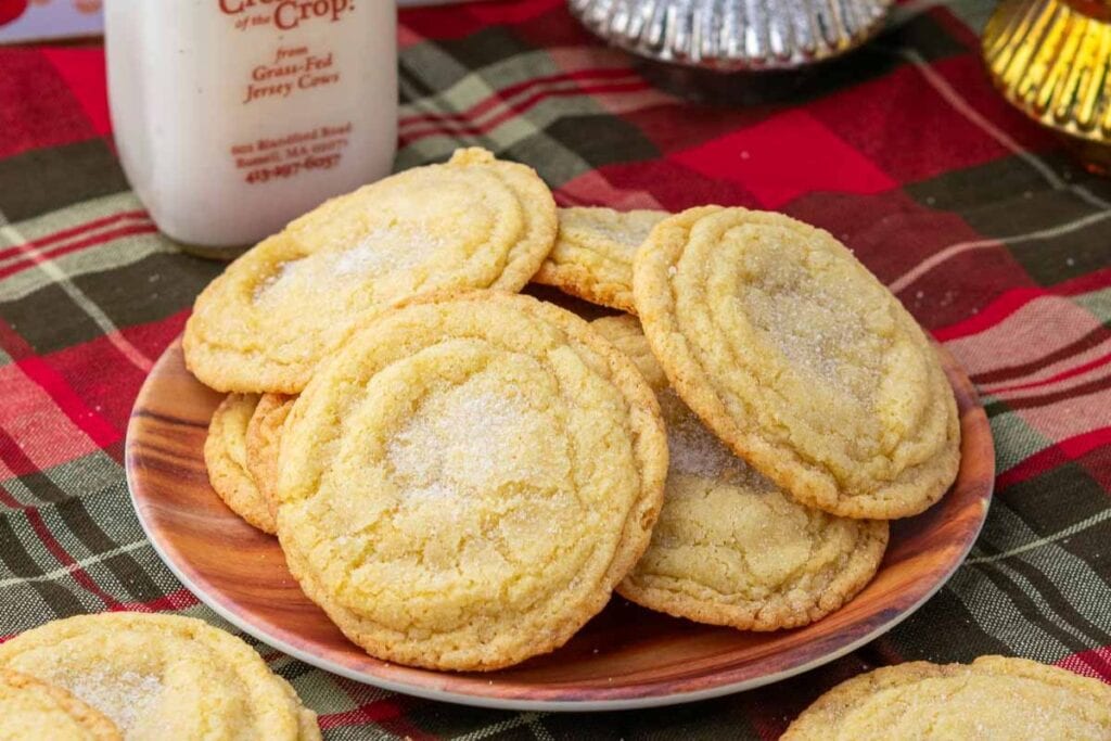 Sugar-covered cookies on a wooden plate with a bottle of milk and plaid tablecloth.