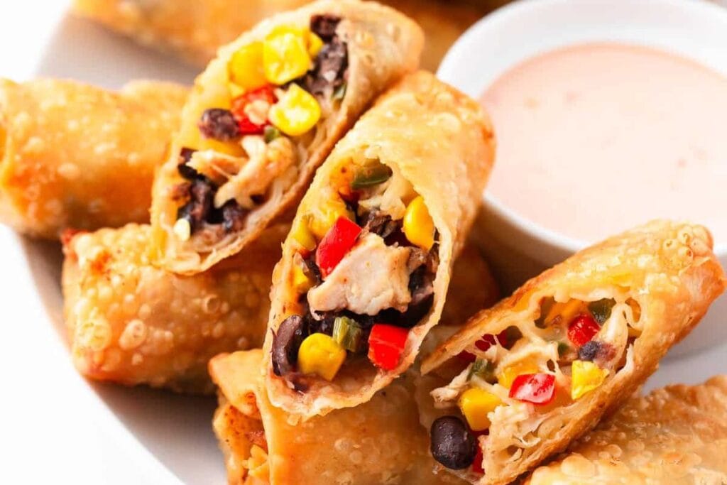 Close-up of Southwestern egg rolls with dipping sauce on a white plate.