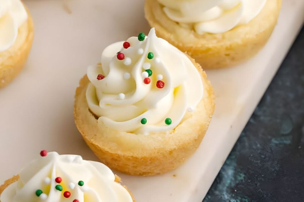 Mini sugar cookie cups filled with white frosting and Christmas sprinkles.