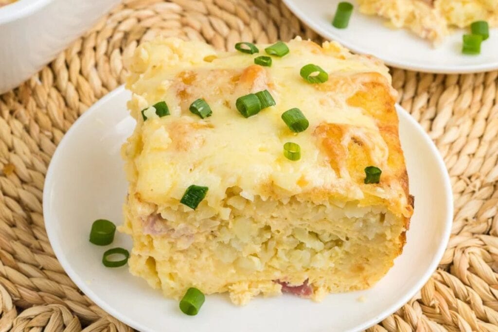 Slice of tater tot casserole on a white plate, garnished with green onions.