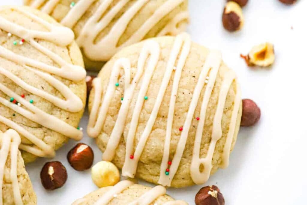 Close-up of iced sugar cookies with sprinkles and hazelnuts on a white surface.