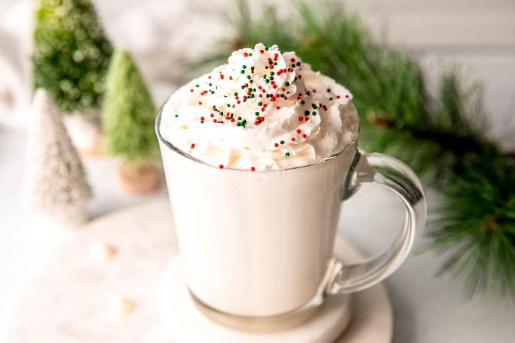 White hot chocolate with whipped cream and sprinkles in a clear mug.
