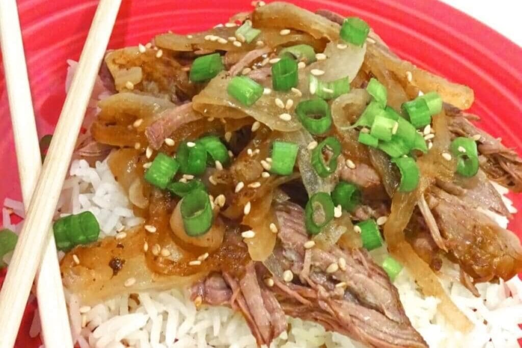 Crockpot asian style beef served over rice on a plate.