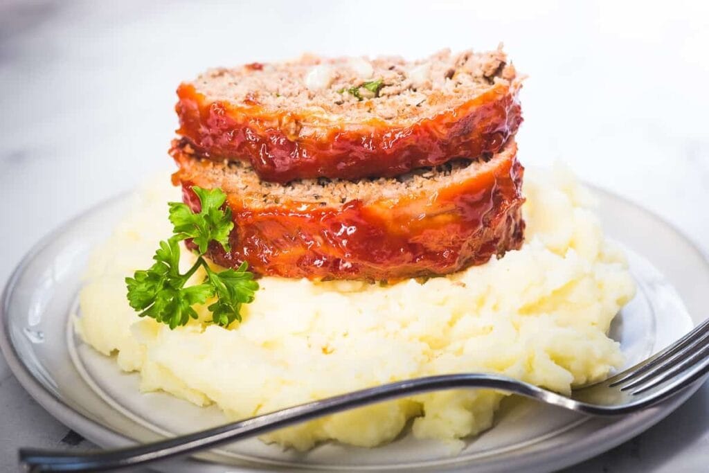 Bacon-wrapped meatloaf served with mashed potatoes on a plate.
