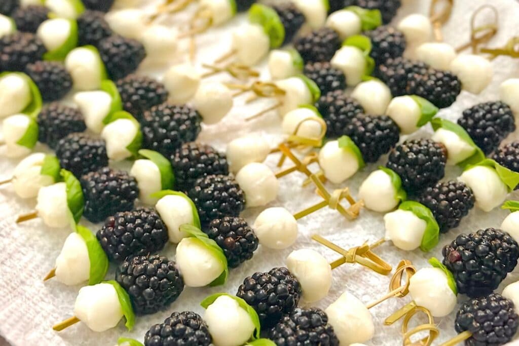 Blackberry, mozzarella, and basil skewers neatly lined on a paper towel.