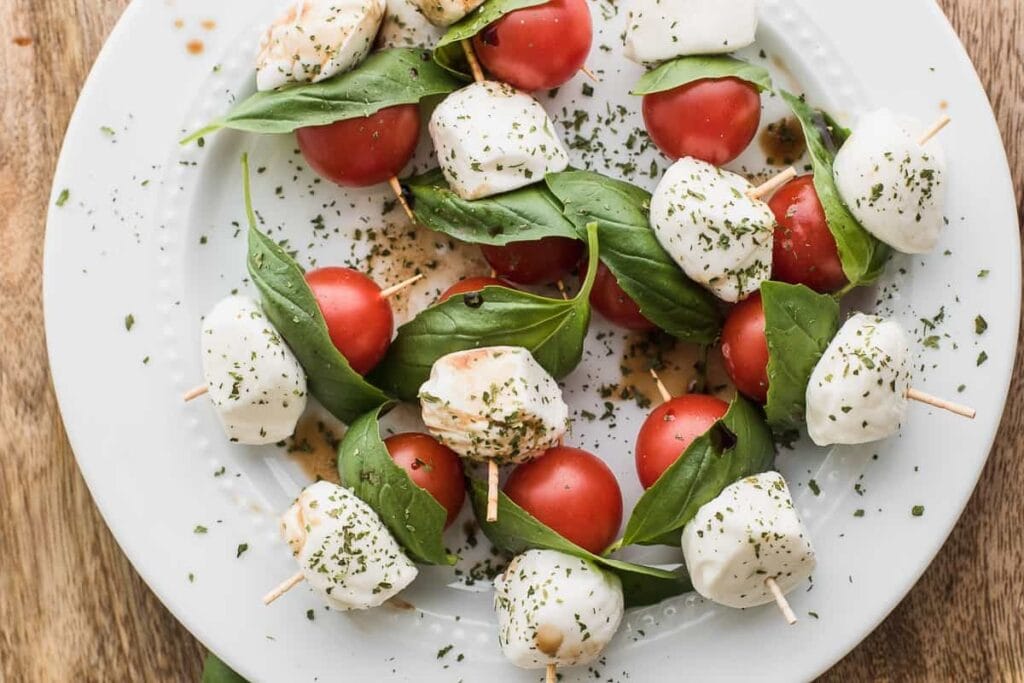 Caprese skewers with basil, mozzarella, and tomatoes on a plate.